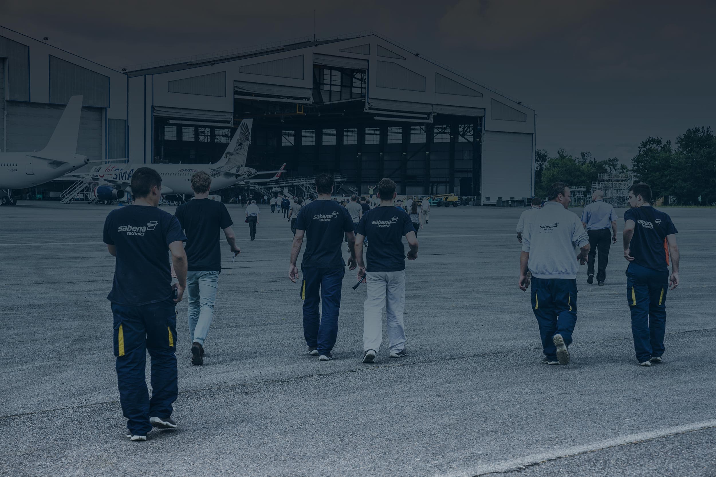 Équipe de techniciens Sabena technics marchant vers un hangar, sur la piste d’un site de maintenance aéronautique